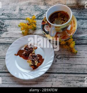 The delicious traditional Italian dessert called mimosa covered in liquid chocolate with a cup of barley coffee and yellow sedum flowers Stock Photo