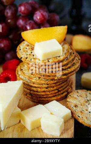 Cheddar cheese, creckers and fruits on wooden board Stock Photo