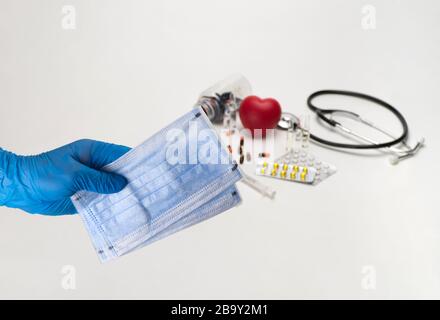 Hand holding a medical mask against the background of a stethoscope and tablets. Coronavirus Protection Concept Stock Photo