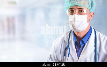 Doctor in his forties with face protection such as a mask, glasses and cap, dressed in a white uniform with a stethoscope hanging from his neck in hos Stock Photo