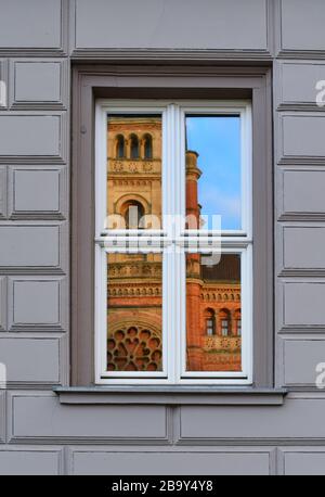 Window pane of a house with grey bricks. An old church is reflecting in the glass of the window pane. Blue sky. Stock Photo