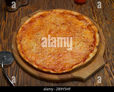 Pizza on a wooden tray, tomatoes, cheese, olive oil in a glass decanter on a wooden table Stock Photo