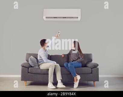 The young couple turns on the air conditioner cools the air while sitting on the sofa in the room. Stock Photo
