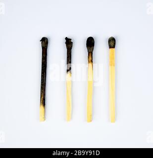 Four burned matches arranged in a row showing the stages of a match burnt before a white background Stock Photo