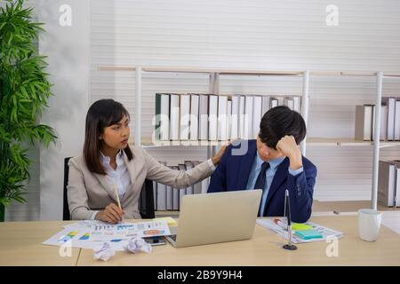 An Asian female leader comforted and cheered on a sad-looking male employee. Stock Photo