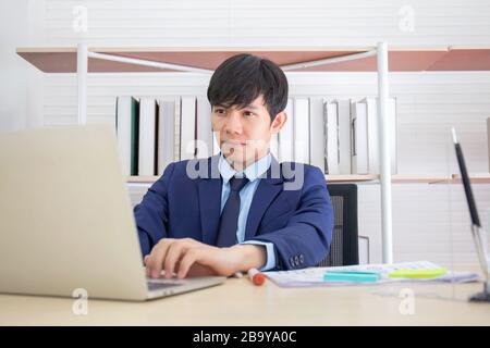 A young Asian businessman sat seriously on the desk in the office.