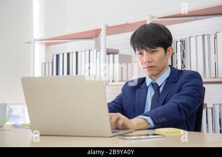 A young Asian businessman sat seriously on the desk in the office. Stock Photo