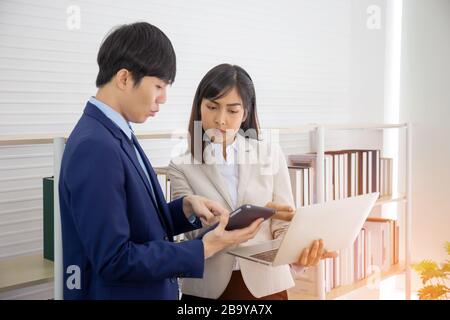 Two young Asian businessmen stand meeting in the office in the hand of the tablet. Stock Photo