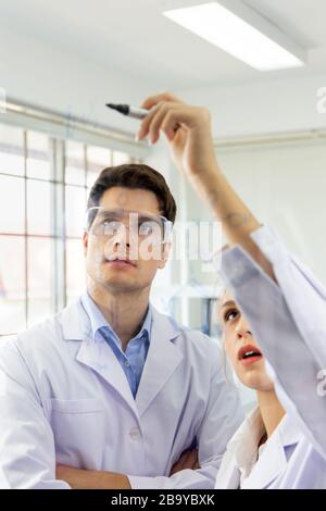 Close-up, a group of scientists, young women and young men are recording formulas on a glass board. Stock Photo