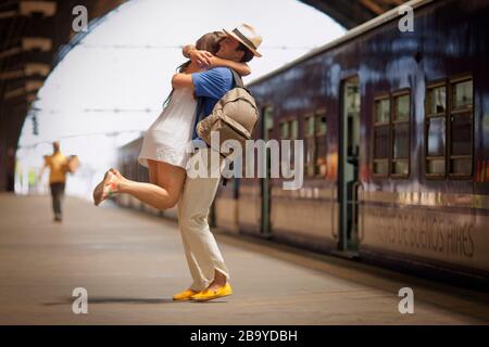 Young heterosexual couple embrace on the platform of an arched railway station. Stock Photo