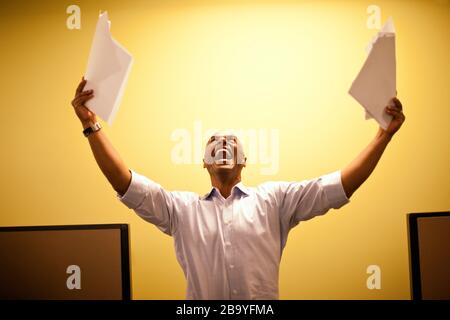 Man shouts throwing paper into the air arms raised. Stock Photo