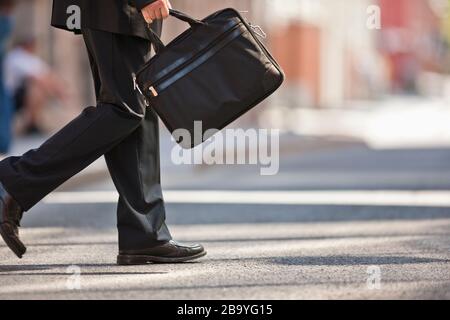 Businessman in a suit and holding a briefcase leaps into the air in a narrow empty street. Stock Photo