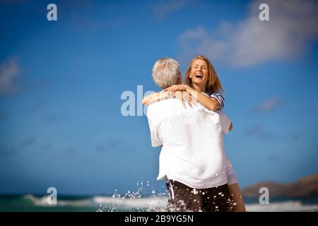 Man carrying his laughing wife into water. Stock Photo