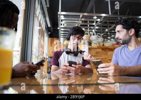 Group of young people of different ethnicities sitting at the table of a cafeteria drinking fruit juice using the mobile Stock Photo