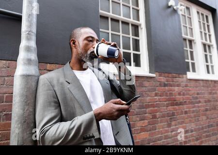 African American man drinking takeaway coffee and using his phone Stock Photo