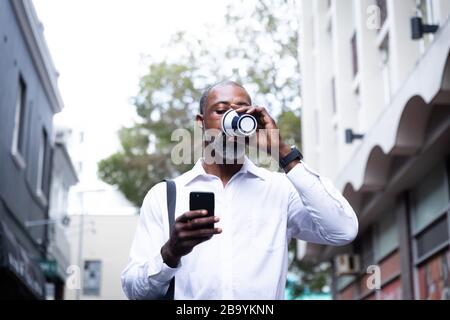 African American man drinking takeaway coffee and using his phone Stock Photo