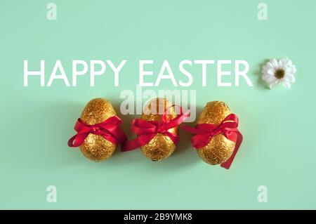 Three chocolate easter eggs tied with red silk ribbon and happy easter greeting Stock Photo