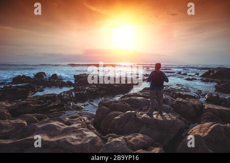 Seascape in the evening. The rocky coast. Silhouette of a man on the beach who is watching the magical sunset Stock Photo