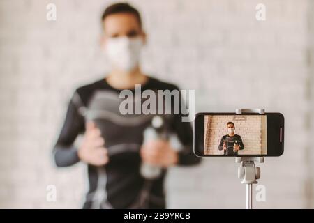 Filming online classes with confident professional fitness trainer. Exercising at home during coronavirus quarantine. Young sports man blogger in medi Stock Photo