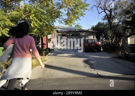 Asian woman wearing a pink sweater walking down a driveway with a tote bag around shoulder. Stock Photo