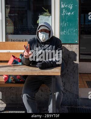 Man wearing a facemark doing a V for Victory sign while resting on a bench outside a closed restaurant in central Berlin during the corona crisis Stock Photo