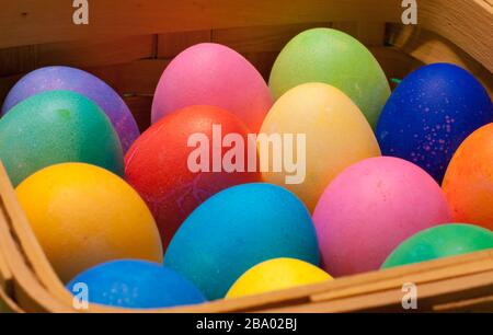 Side view of a wooden basket containing red, orange, yellow, green, blue and pink dyed eggs