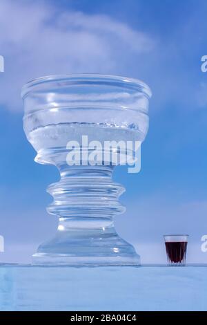 A large ice cup and a small glass with red wine are standing against the blue sky. Bowl and tincture stand on an ice plate. Stock Photo