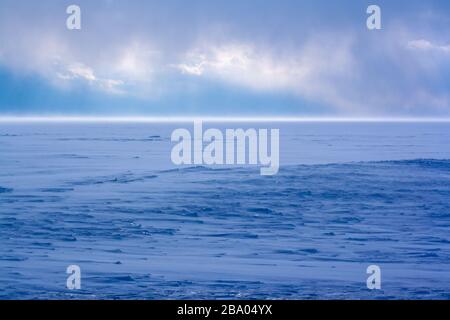 A strong snowstorm on Lake Baikal in winter. No ice is visible. A lot of snow. The sun shines through the clouds. Strong wind sweeps snow. Blue color Stock Photo