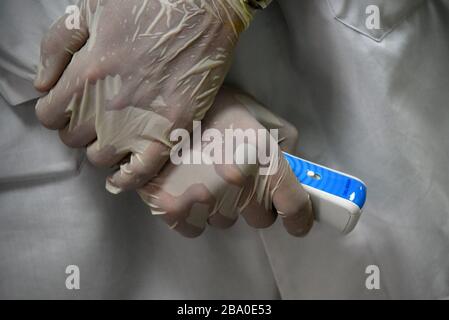 Hands in rubber medical gloves holding the pyrometer to measure the temperature of patients in clinic, Astrakhan, Russia. Stock Photo