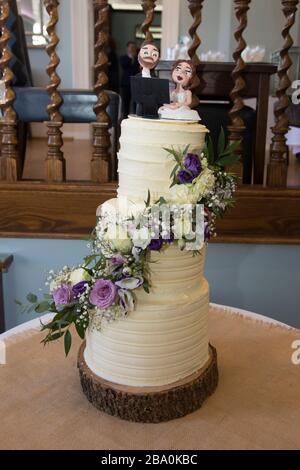 Three tier wedding cake decorated with real flowers and covered in cream butter icing on a couples wedding day Stock Photo