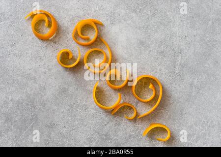 Orange fruit peeled skin curls on stone grey background. Abstract diagonal composition with soft light. Stock Photo