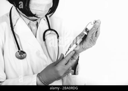 Close up of a doctor in white lab coat and medical mask on white background holds syringe and medicine in ampoule. Black and white photo. Stock Photo