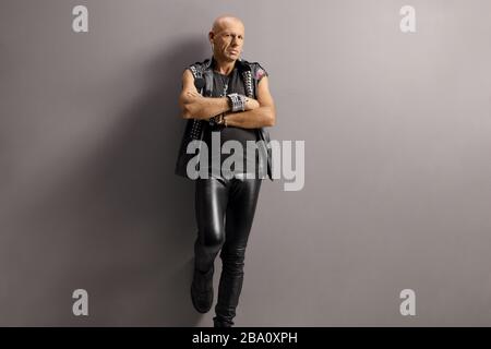 Middle aged punk man leaning on a gray wall with crossed arms Stock Photo