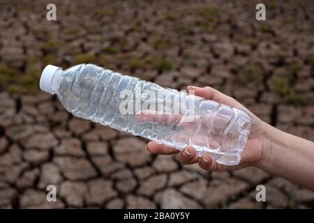 Close up woman hand holding the clear plastic bottle at crack soil background, These waste come from urban and industrial areas can not get rid of Stock Photo