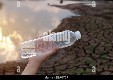 Close up woman hand holding the clear plastic bottle at crack soil background, These waste come from urban and industrial areas can not get rid of Stock Photo