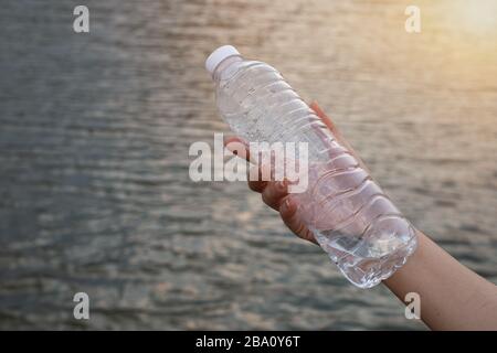 Close up woman hand holding the clear plastic bottle at river background Stock Photo
