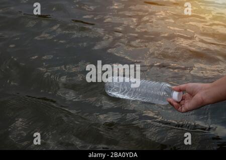 Woman hand to pick up the used waste plastic bottle on the water in a canal Stock Photo