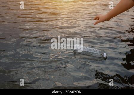 Woman hand to pick up the used waste plastic bottle on the water in a canal Stock Photo