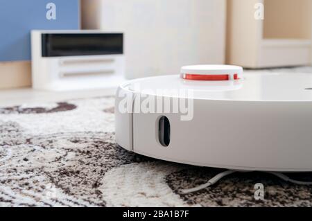 White round robotic vacuum cleaner on fitted carpet floor Stock Photo