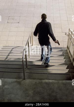 Rear View of Man with Gun walking down Steps Stock Photo