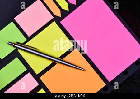 Metal pen on a block of bright multicolored stickers on a black background Stock Photo