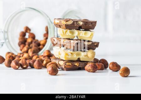 White and dark nut chocolate with hazelnuts on white table. Stock Photo