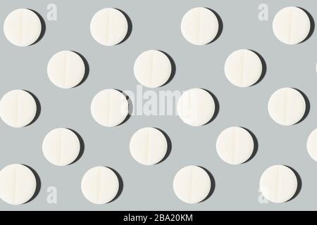 Pattern with white pills with a line in the middle on a gray background, texture of pills. Stock Photo