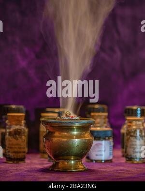 Smoke of burning white sage on an incense burner with more little bottles in the background Stock Photo