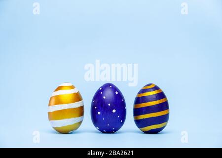 Three easter trendy colored classic blue and golden decorated eggs striped pattern on blue. Happy Easter card with copy space for text. Minimal style Stock Photo