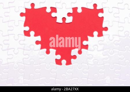 Heart from white puzzles as a symbol of love on a red background. Fans like puzzles that complement each other Stock Photo