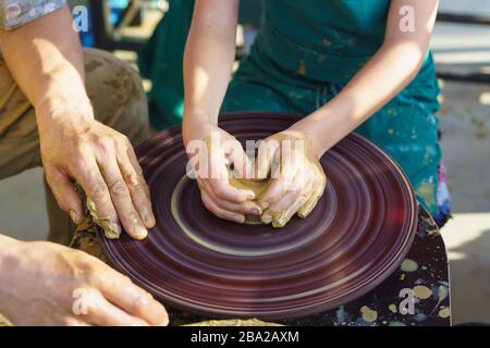 Master and student. Childrens hands in the yellow clay on the rotating Potters wheel molded the dishes. Craft Stock Photo