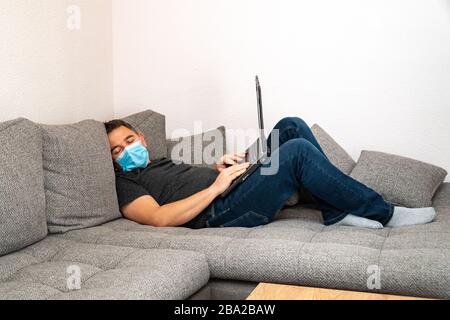 Quarantined coronavirus man in medical mask is tired and sleeping on the couch. Self-isolation pandemic COVID19 Stock Photo