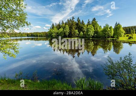 Scenic view of a Kladska lake in the Czech Republic, close to Marianske Lazne surrounded with forest. Sunny summer landscape with blue sky and clouds. Stock Photo