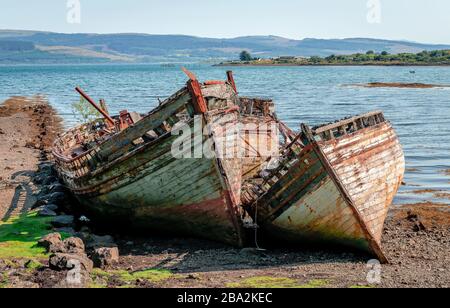 Beautiful seascape with three semi-destroyed old fishing boat in the beach and the Sound of Mull in the background. Isle of Mull, Scotland, August 201 Stock Photo